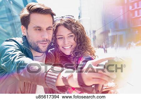 Portrait of young attractive man taking selfie with his girlfriend in the middle of the city with lens flare in background View Large Photo Image Picture - Portrait of young attractive man taking selfie with his girlfriend in the middle of the city with lens flare in background. Fotosearch