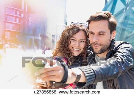 Stock Photograph - Portrait of young attractive man taking selfie with his girlfriend in the middle of the city. Fotosearch