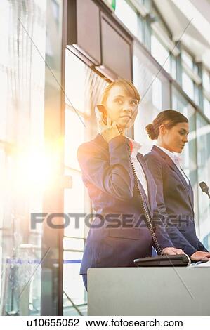 Stock Image - Portrait of young attractive passenger service agent talking on telephone while standing in airport gate. Fotosearch