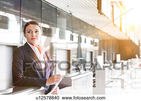 Stock Image - Portrait of young attractive passenger service agent holding boarding pass in airport check in area. Fotosearch