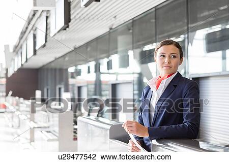 Stock Image - Portrait of young attractive passenger service agent holding boarding pass in airport check in area. Fotosearch