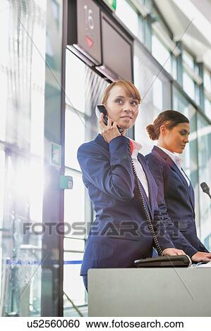 Stock Image - Portrait of young attractive passenger service agent talking on telephone while standing in airport gate. Fotosearch