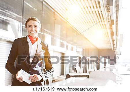 Portrait of young attractive passenger service agent holding boarding pass in airport check in area View Large Photo Image Stock Photo - Portrait of young attractive passenger service agent holding boarding pass in airport check in area. Fotosearch