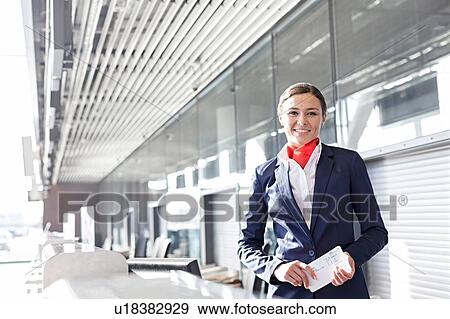 Stock Photo - Portrait of young attractive passenger service agent holding boarding pass in airport check in area. Fotosearch