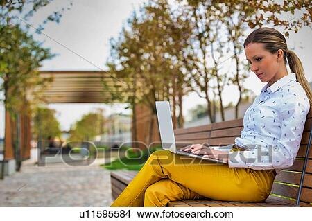 Portrait of young attractive businesswoman sitting while working on her laptop and sitting on bench View Large Photo Image Picture - Portrait of young attractive businesswoman sitting while working on her laptop and sitting on bench. Fotosearch