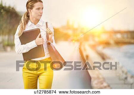 Portrait of Young attractive businesswoman walking while holding document View Large Photo Image Picture - Portrait of Young attractive businesswoman walking while holding document. Fotosearch