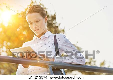 Picture - Portrait of young attractive businesswoman using digital tablet while leaning on railing. Fotosearch