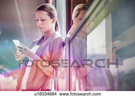 Portrait of young attractive businesswoman using smartphone while leaning on window View Large Photo Image Picture - Portrait of young attractive businesswoman using smartphone while leaning on window. Fotosearch