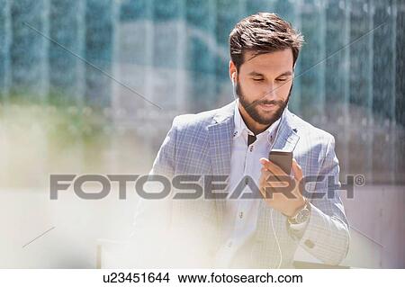 Picture - Portrait of young attractive businessman using smartphone with earphones on. Fotosearch