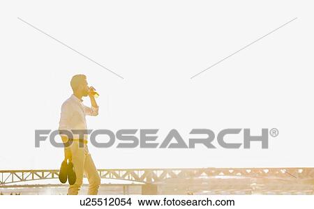 Portrait of young attractive businessman drinking beer and walking barefoot on the beach while holding his shoes View Large Photo Image Picture - Portrait of young attractive businessman drinking beer and walking barefoot on the beach while holding his shoes. Fotosearch