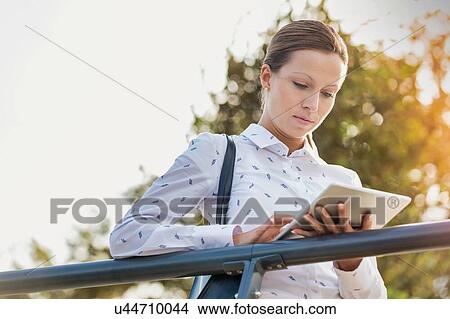 Portrait of young attractive businesswoman using digital tablet while leaning on railing View Large Photo Image Picture - Portrait of young attractive businesswoman using digital tablet while leaning on railing. Fotosearch