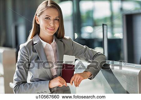 Stock Image - Portrait of young attractive businesswoman holding her passport and boarding pass in airport. Fotosearch