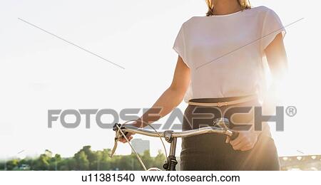 Stock Image - Portrait of young attractive businesswoman holding bicycle while walking on the beach . Fotosearch