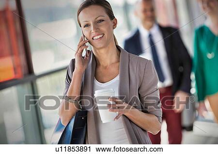 Portrait of young attractive businesswoman talking on smartphone and holding cup of coffee while walking against colleague View Large Photo Image Stock Image - Portrait of young attractive businesswoman talking on smartphone and holding cup of coffee while walking against colleague. Fotosearch