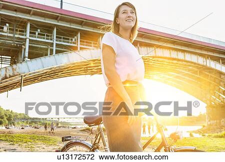 Stock Image - Portrait of young attractive businesswoman holding bicycle while walking under the bridge. Fotosearch