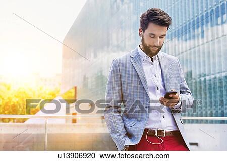 Stock Image - Portrait of young attractive businessman using smartphone with earphones on. Fotosearch