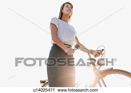 Stock Image - Portrait of young attractive businesswoman holding bicycle while walking on the beach . Fotosearch