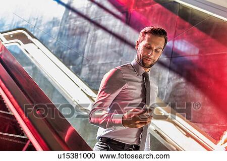 Stock Image - Portrait of young attractive businessman using smartphone while walking downstairs. Fotosearch