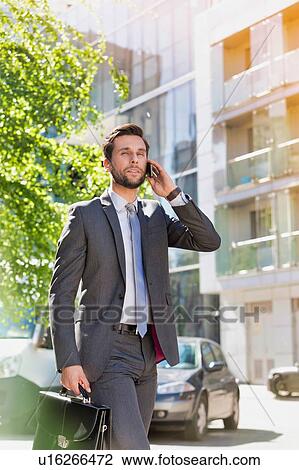 Portrait of young attractive businessman walking while talking on smartphone View Large Photo Image Stock Image - Portrait of young attractive businessman walking while talking on smartphone. Fotosearch