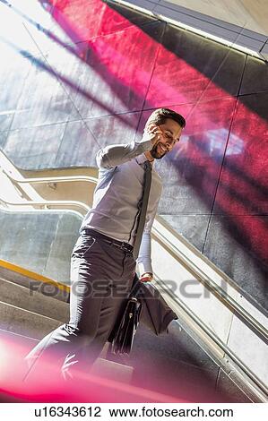 Portrait of young attractive businessman talking on smartphone while walking downstairs View Large Photo Image Stock Image - Portrait of young attractive businessman talking on smartphone while walking downstairs. Fotosearch