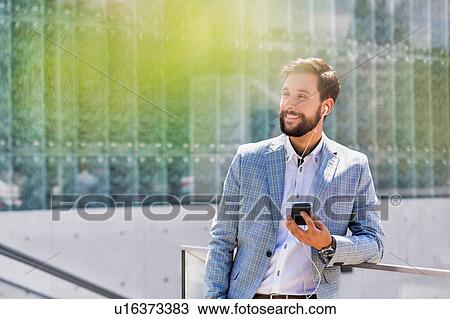 Portrait of young attractive businessman using smartphone with earphones on View Large Photo Image Stock Image - Portrait of young attractive businessman using smartphone with earphones on. Fotosearch