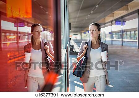 Stock Image - Portrait of young attractive businesswoman holding cup of coffee while walking. Fotosearch
