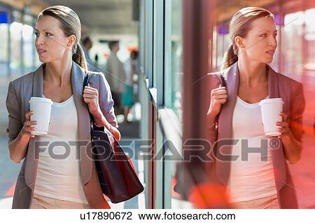 Stock Image - Portrait of young attractive businesswoman holding cup of coffee while walking. Fotosearch