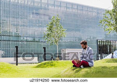 Stock Image - Portrait of young attractive businessman using digital tablet while sitting on the grass. Fotosearch