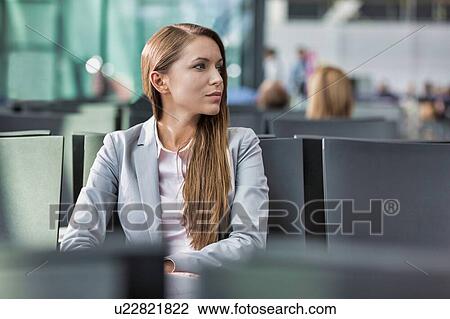 Stock Image - Portrait of young attractive businesswoman sitting while waiting in her gate for boarding at airport. Fotosearch