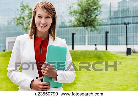 Portrait of young attractive businesswoman standing while holding document View Large Photo Image Stock Image - Portrait of young attractive businesswoman standing while holding document. Fotosearch