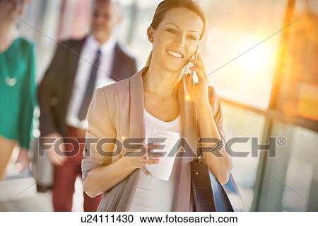 Portrait of young attractive businesswoman talking on smartphone and holding cup of coffee while walking against colleague View Large Photo Image Stock Image - Portrait of young attractive businesswoman talking on smartphone and holding cup of coffee while walking against colleague. Fotosearch