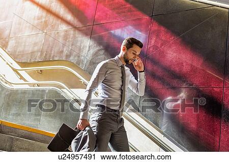 Stock Image - Portrait of young attractive businessman talking on smartphone while walking downstairs. Fotosearch