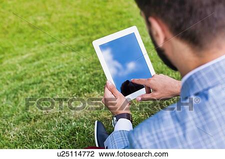 Portrait of young attractive businessman using digital tablet while sitting on the grass View Large Photo Image Stock Image - Portrait of young attractive businessman using digital tablet while sitting on the grass. Fotosearch