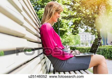 Portrait of young attractive businesswoman sitting on bench while working on her laptop View Large Photo Image Stock Image - Portrait of young attractive businesswoman sitting on bench while working on her laptop. Fotosearch