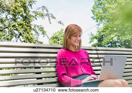 Portrait of young attractive businesswoman sitting on bench while working on her laptop View Large Photo Image Stock Image - Portrait of young attractive businesswoman sitting on bench while working on her laptop. Fotosearch