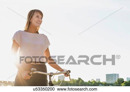 Stock Image - Portrait of young attractive businesswoman holding bicycle while walking on the beach . Fotosearch