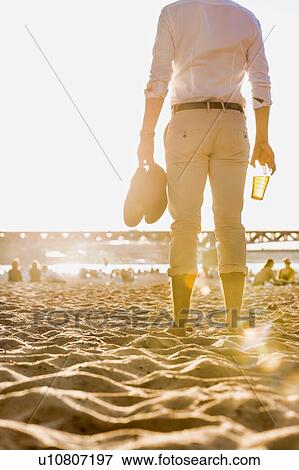 Portrait of young attractive businessman drinking beer and walking barefoot on the beach while holding his shoes View Large Photo Image Stock Photo - Portrait of young attractive businessman drinking beer and walking barefoot on the beach while holding his shoes. Fotosearch