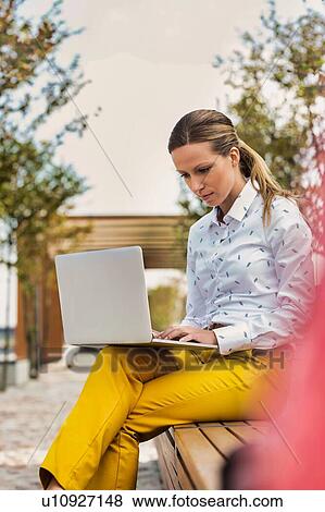 Stock Photo - Portrait of young attractive businesswoman sitting while working on her laptop and sitting on bench. Fotosearch