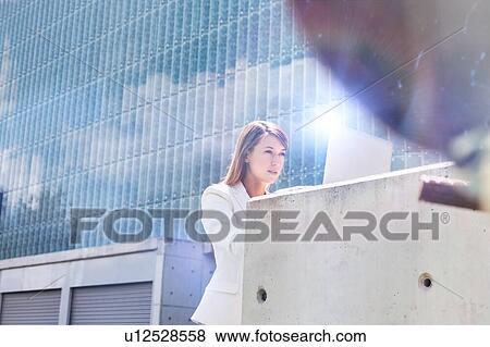 Stock Photo - Portrait of young attractive businesswoman working on her laptop outdoor. Fotosearch