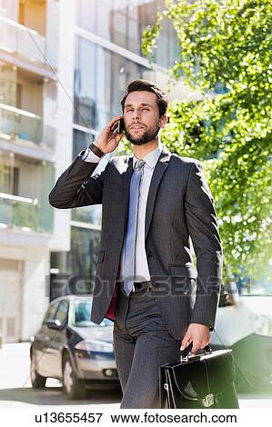 Portrait of young attractive businessman walking while talking on smartphone View Large Photo Image Stock Photo - Portrait of young attractive businessman walking while talking on smartphone. Fotosearch