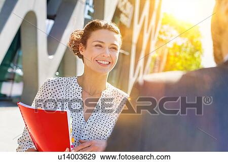 Stock Photo - Portrait of young attractive businesswoman smiling while talking to colleague. Fotosearch