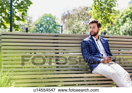 Stock Photo - Portrait of young attractive businessman using smartphone while sitting on bench. Fotosearch