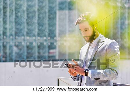 Stock Photo - Portrait of young attractive businessman using smartphone with earphones on. Fotosearch