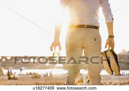 Portrait of young attractive businessman drinking beer and walking barefoot on the beach while holding his shoes View Large Photo Image Stock Photo - Portrait of young attractive businessman drinking beer and walking barefoot on the beach while holding his shoes. Fotosearch