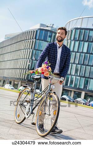 Stock Photo - Portrait of young attractive businessman standing with his bicycle while holding boquet of flowers. Fotosearch