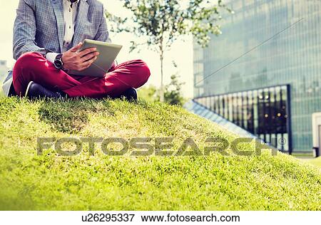 Portrait of young attractive businessman using digital tablet while sitting on the grass View Large Photo Image Stock Photo - Portrait of young attractive businessman using digital tablet while sitting on the grass. Fotosearch
