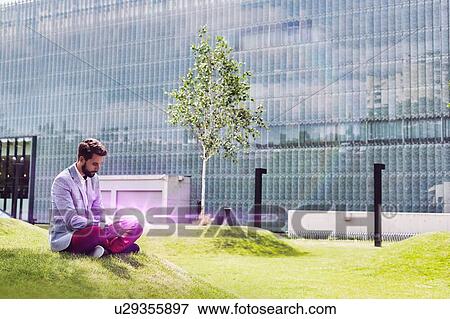 Portrait of young attractive businessman using digital tablet while sitting on the grass View Large Photo Image Stock Photo - Portrait of young attractive businessman using digital tablet while sitting on the grass. Fotosearch