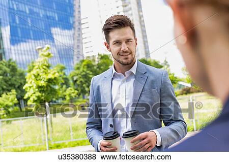 Stock Photo - Portrait of young attractive businessman holding two cups of coffee . Fotosearch