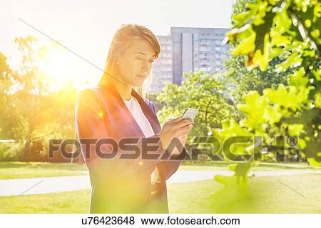 Stock Photo - Portrait of young attractive businesswoman using smartphone in park. Fotosearch