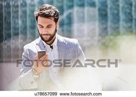 Stock Photo - Portrait of young attractive businessman using smartphone with earphones on. Fotosearch